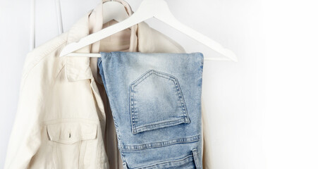 Jeans and a denim jacket hang on a clothes hanger. Casual clothes on a white background.