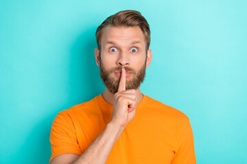 Photo of excited silent astonished man with blond hairstyle dressed orange t-shirt finger on lips mouth isolated on teal color background