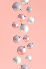 Creative scene made of baubles falling against pastel pink background. Minimal New Year concept. Christmas card layout. Holiday aesthetic.
