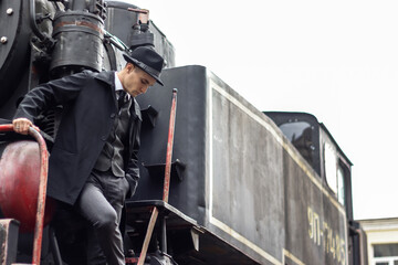 Men's photo session in a classic plaid suit and hat against the backdrop of an old steam locomotive.
