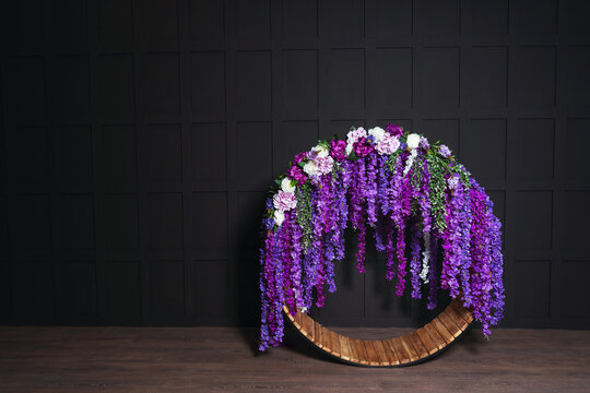 round swing with purple flowers against a dark wall. wedding iron swing with a wooden seat in a photo studio. wedding photo zone with indoor swing