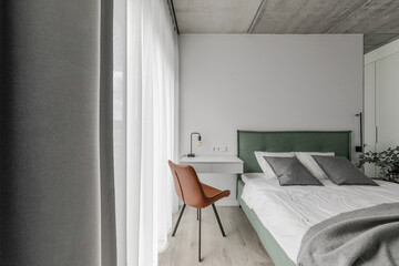 Modern minimalistic bedroom interior design in grey shades with light green bed, leather chair, eucalyptus in glass vase. Scandinavian style.  Aesthetic simple interior design concept.