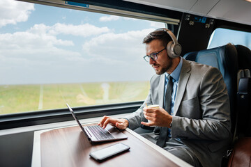Handsome middle age businessman using his laptop computer while traveling with high-speed train. Modern and fast travel concept. - Powered by Adobe