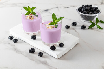 Blackberry milkshake or smoothie in two glass glasses on a white wooden board and marble table. the concept of healthy eating.