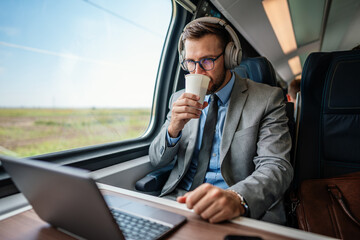 Handsome middle age businessman using his laptop computer while traveling with high-speed train. Modern and fast travel concept.