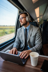 Handsome middle age businessman using his laptop computer while traveling with high-speed train. Modern and fast travel concept. © Dusko