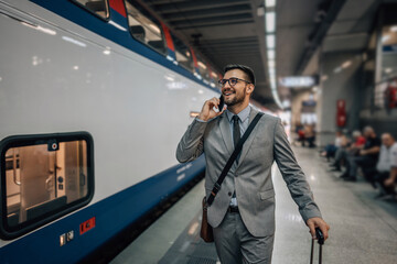 Handsome middle age businessman with suitcase standing in station platform and waiting for...