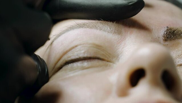 A special needle tattoo machine makes a permanent make-up correction of a woman's eyebrows. Microblading, powder coating close-up.