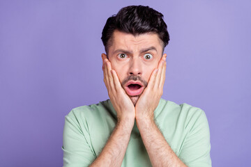 Photo of scared unhappy handsome guy with brunet hairstyle stubble wear t-shirt palms on cheekbones isolated on purple color background