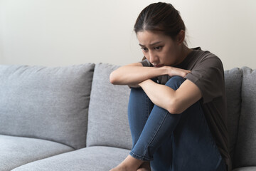 Unhappy anxiety young Asian woman covering her face with pillow on the cough in the living room at home.