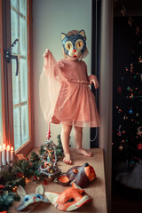 Cute little girl is dressing up a tiny Christmas tree and trying on New Year's animal masks. Image with selective focus and toning. 