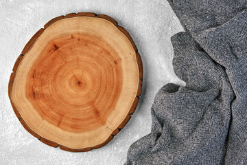 Wooden cutting board or dish coaster and gray kitchen towel on a light gray concrete table