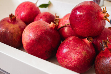 Many large red pomegranates are washed in the sink