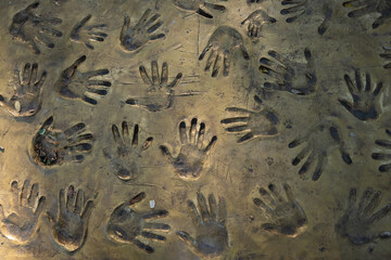 Handprints of people on a clay or concrete surface painted in gold color