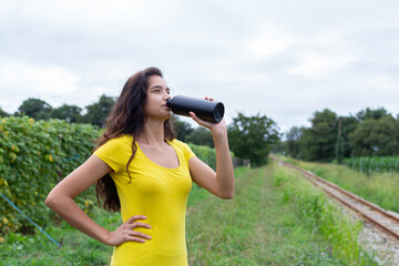 Young ethnic female athlete drinking water after training in nature 