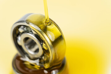 Closed up macro, Pouring automotive engine oil into ball bearing isolated on yellow oil background with copy space, engineering and industrial concept. Motor oil on bearing - obrazy, fototapety, plakaty