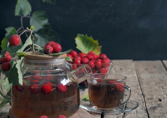 Tea with fresh and dried hawthorn berries in a glass cup on a wooden ancient background. Medicinal soothing herbal tea. Space for text. Alternative medicine concept.