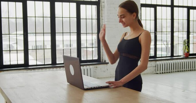 Female dance instructor teaching online dance class via video using laptop for online communication saying hello to student