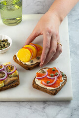 woman hand pick up toast with dark rye bread, herrings, smoked salmon and capers. copy space. Vertical