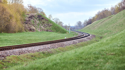 Selective focus railway track twists and turns between hills. Empty rounding and turning single track of railways. Shallow focus perspective view of rounded rails bend horizontal 16x9.