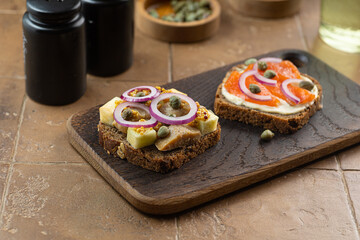 Toasts with dark rye bread, herring, pickled capers, salmon on black cutting board
