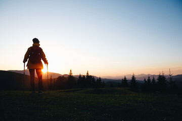 Fototapeta na wymiar Hiker with backpack standing on top of a mountain and enjoying sunset. Woman successful hiking silhouette in mountains, motivation and inspiration in beautiful sunset