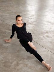 Modern female dancer wearing black outfit lying on the floor doing stretching exercise while practicing in studio - 541452343