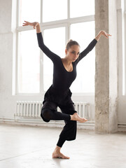 Modern female dancer in black outfit balancing on one leg while practices in a dance studio - 541452364