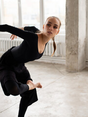 Modern female dancer in black outfit balancing on one leg while practices in a dance studio - 541452368