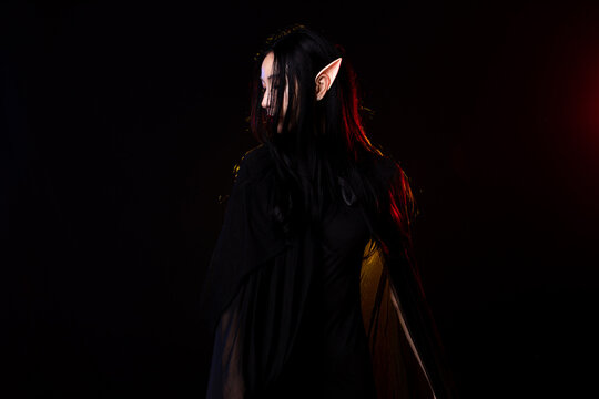 Fairy woman elf queen in black fantasy rope long dress cast spell flowing around witch. Princess girl sharp ears with beautiful face. old style cave. Spell dark magic over black background isolated