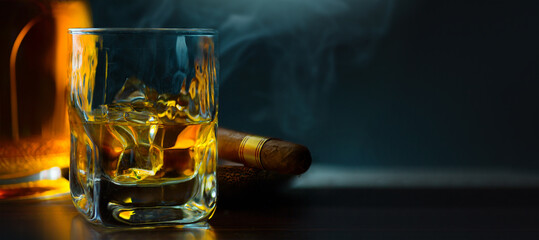 A glass of whiskey with ice and a Cuban cigar on a wooden table on a dark background. Men's club banner idea. Copy space for text - obrazy, fototapety, plakaty