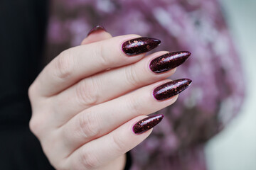 Woman hand with long nails and a bottle of dark purple burgundy nail polish