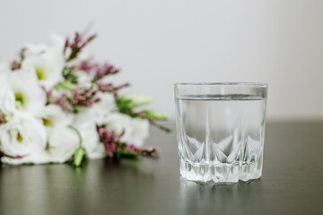 Glass of clean water on table near flowers. Concept for drinks, healthy lifestyle and diet.