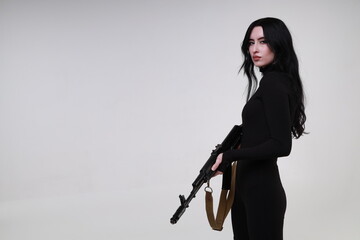 Beautiful slender brunette woman in black clothes with assault rifle