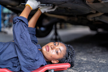 Mechanical girl dirty face wearing overall cover suit lay on garage creeper trolley tighten bolt under car at the car repair shop