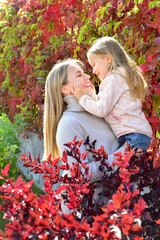 Mother and daughter on a walk. Autumn season. Bright autumn leaves. Sunny day. Happy family outdoors - 541461106