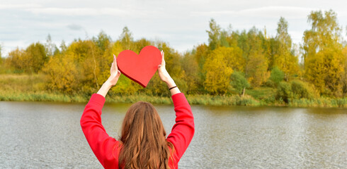 Beautiful woman holding a red heart over autumn nature background. Portrait stylish pretty woman outdoor. - 541461145