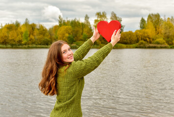 Beautiful woman holding a red heart over autumn nature background. Portrait stylish pretty woman outdoor. - 541461172