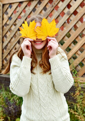 Beautiful smiling redhead teen girl with maple yellow leaves over wooden background. Autumn time. Fall season. knitted sweater - 541461177