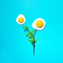 Fried eggs as spring flowers, creative Easter inspired layout against bright blue background.