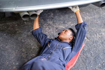 Mechanical girl dirty face wearing overall cover suit lay on garage creeper trolley tighten bolt...