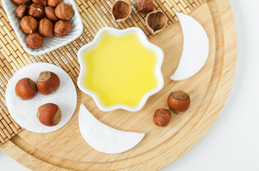 Hazelnut oil in a small white bowl, wooden hair comb and cotton eye patches. Homemade face or hair mask, facial cleanser, natural beauty treatment and spa recipe. Top view, copy space.