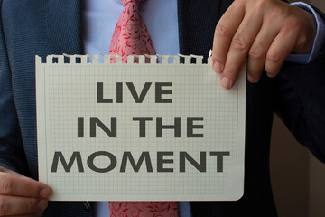 The paper in the hand of the man in the suit reads ''live in the moment''.