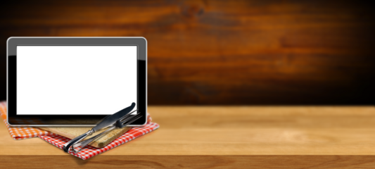 Blank digital tablet computer with white or transparent screen for recipes or food menu. On a wooden kitchen counter with a cutting board, checkered tablecloth and silver cutlery. Png.
