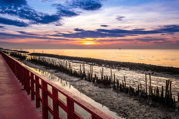 Fototapeta premium A long red wooden bridge, Wooden bridge of nature trail to see the sea, Beautiful sunset, This viewpoint of the sea at Samut Sakhon. Thailand