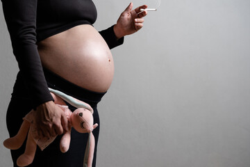 A pregnant woman with a soft toy in her hands smokes a cigarette. The concept of the harm of...