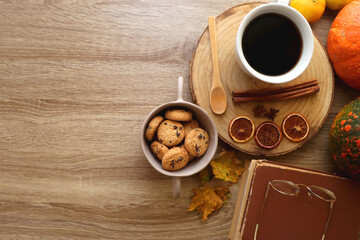 Cup of tea or coffee, seasonal spices, bowl of cookies, blanket, pumpkins, colorful leaves, books and tangerines on wooden table. Cozy hygge at home. Top view.