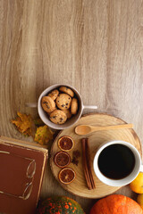 Cup of tea or coffee, seasonal spices, bowl of cookies, blanket, pumpkins, colorful leaves, books and tangerines on wooden table. Cozy hygge at home. Top view.