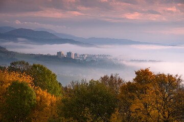 Naklejka na ściany i meble Foggy fall morning near Banska Bystrica. Landscape with forests and mountains around the city. Autumn colored trees at sunrise.