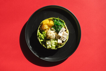 Appetizing bowl with cheese and vegetables sprinkled with sesame seeds on a red background